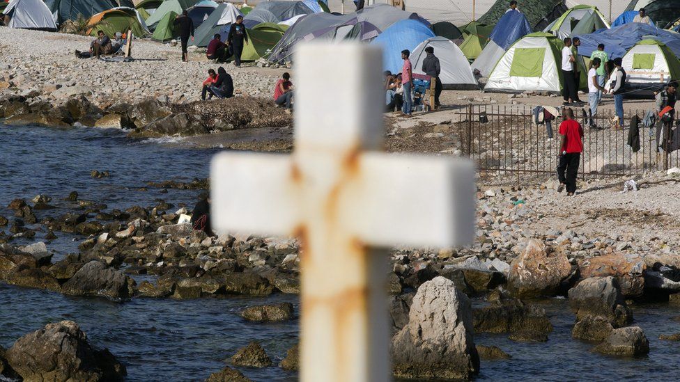 Migrants and refugees are seen on a beach behind a cross in a camp set up by volunteers near the port of Mytilene