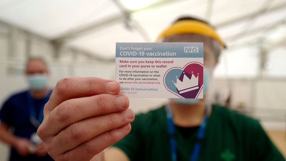medic holding up covid vaccination card