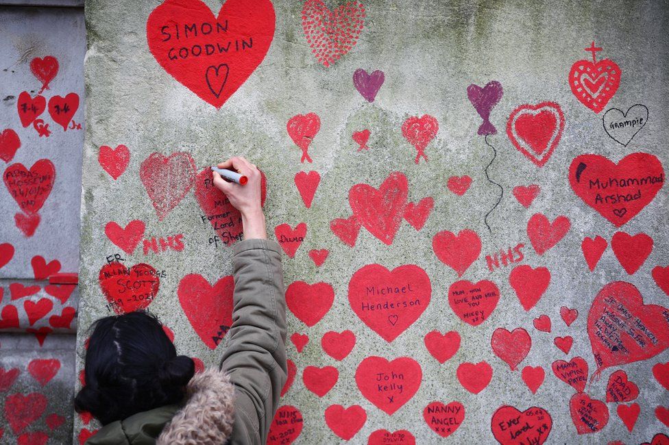 A person paints on the National Covid Memorial wall beside St Thomas' hospital set as a memorial to all those who have died so far in the UK from the coronavirus disease (COVID-19), amid the coronavirus pandemic in London