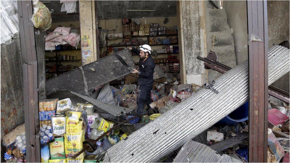 A civil defence member looks for survivors in a damaged shop in the village of Hesh in Idlib province