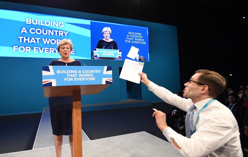 A man holds a piece of paper with P45 written on it as Britain's Prime Minister Theresa May (L) delivers her speech on the final day of Conservative Party Conference in Manchester, Britain, 04 October 2017. The P45 is a reference code for a form on 'Details of employee leaving work' and usually associated with a termination of employment. The conference ran from 01 to 04 of October 2017