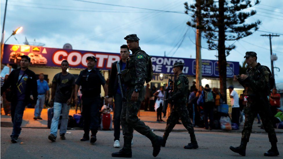 Army soldiers patrol on a street next to people from Venezuela after checking their passports or identity cards at the Pacaraima border control, Roraima state