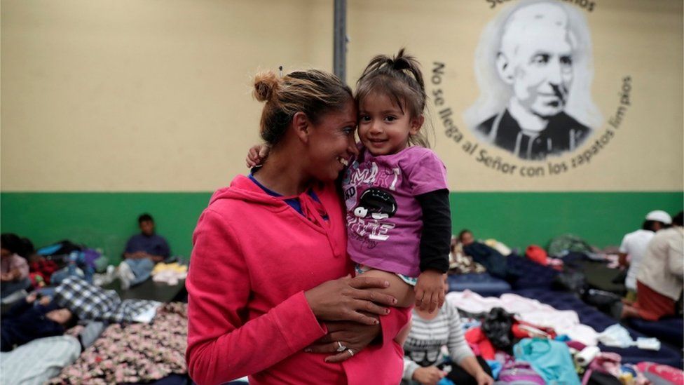 A Honduran migrant, part of a caravan trying to reach the U.S., carries her daughter at a migrant shelter in Guatemala City