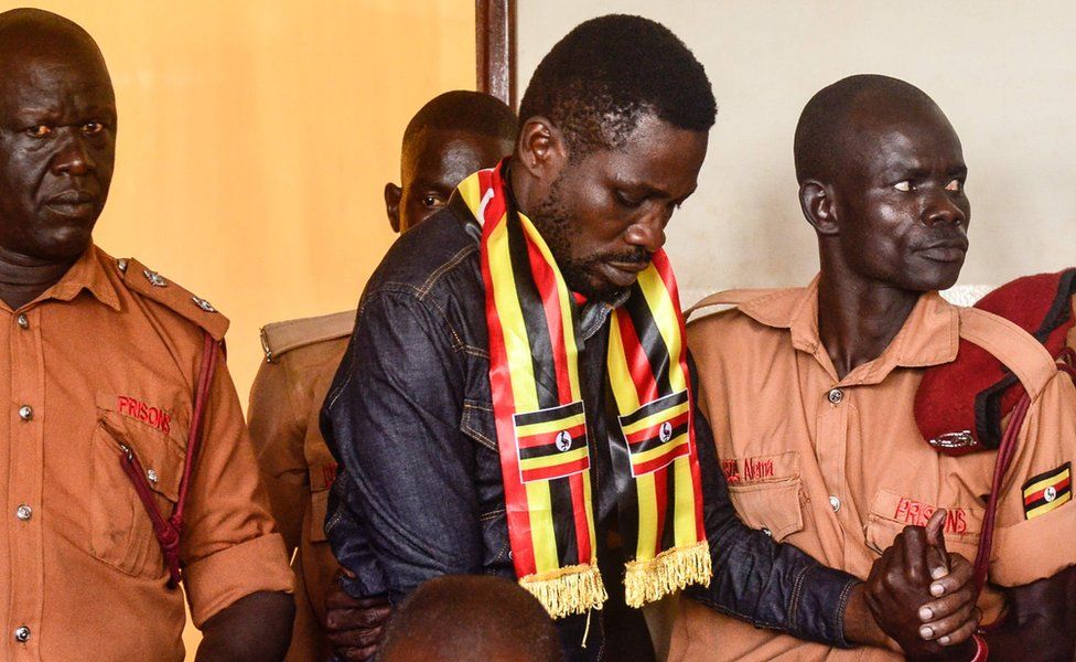 Bobi Wine surrounded by prison guards, one holding his hand, in court in Gulu, northern Uganda - Thursday 23 August 2018