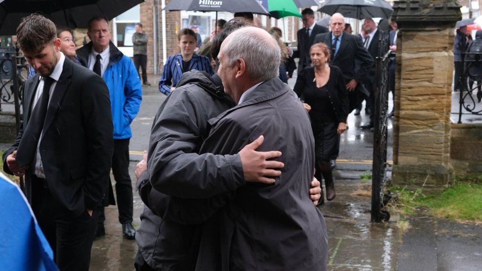 Two men hugging outside Barnaby Webber's funeral