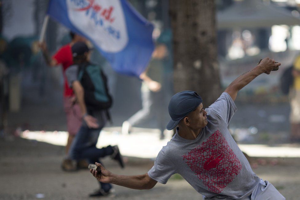 An anti-austerity protester throws a stone at police, outside the state legislature where lawmakers are discussing austerity measures in Rio de Janeiro, Brazil, Tuesday, 6 December