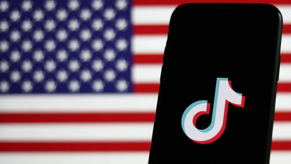 The TikTok logo is displayed on a phone screen with the US flag in the background.
