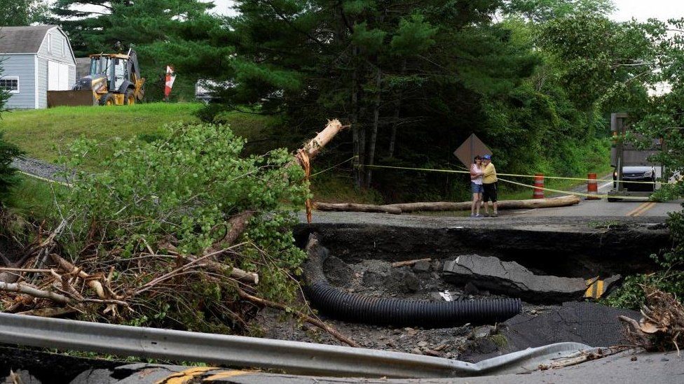 People embrace as they stand near damage to a road, after the heaviest rain to hit the Atlantic Canadian province of Nova Scotia in more than 50 years triggered floods, in Ellershouse, West Hants Regional Municipality, Nova Scotia, Canada July 23, 2023. REUTERS/John Morris