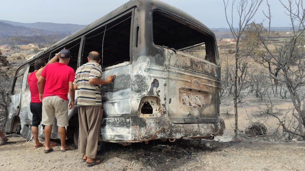 People inspect a burnt vehicle following a wildfire in El Kala, north-eastern Algeria, on 18 August.