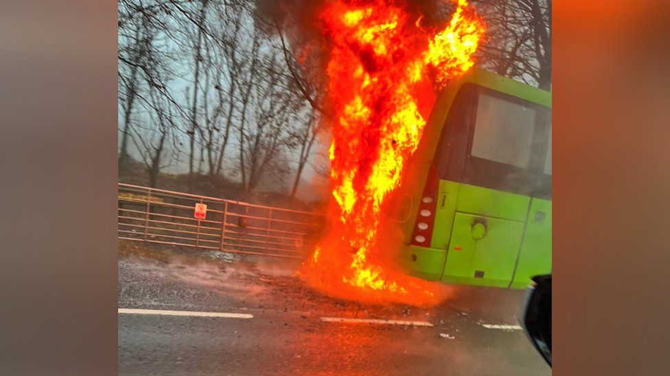 Image of a green bus which is on fire.