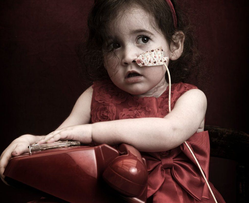 A young girl in a red dress holds a red phone