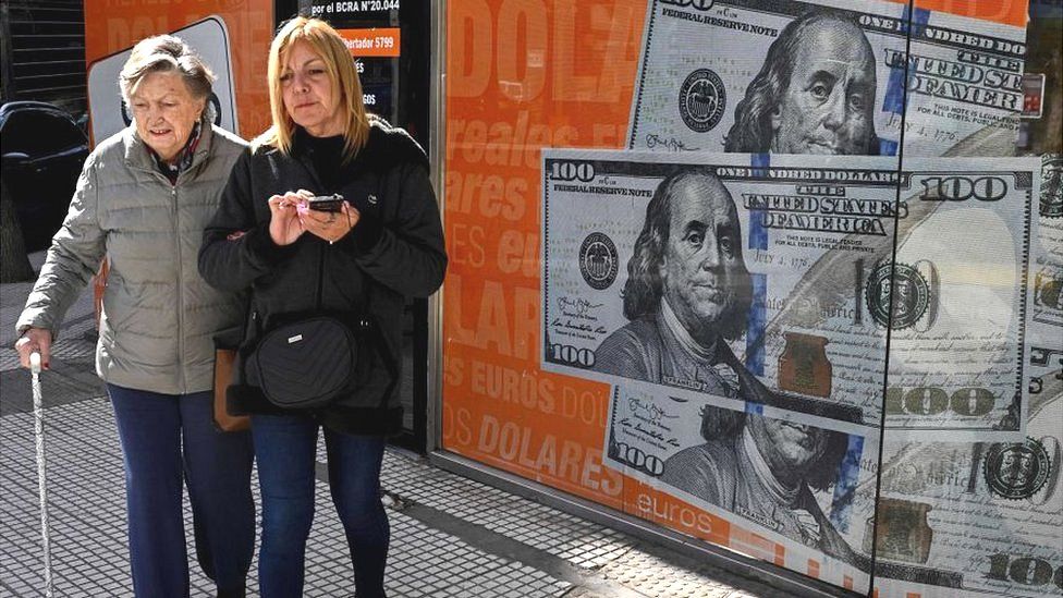 Women in Buenos Aires walk past image of $100 bills, 14 August 2023