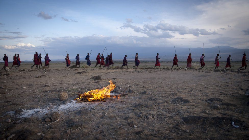 A row of Maasai walk behind a fire