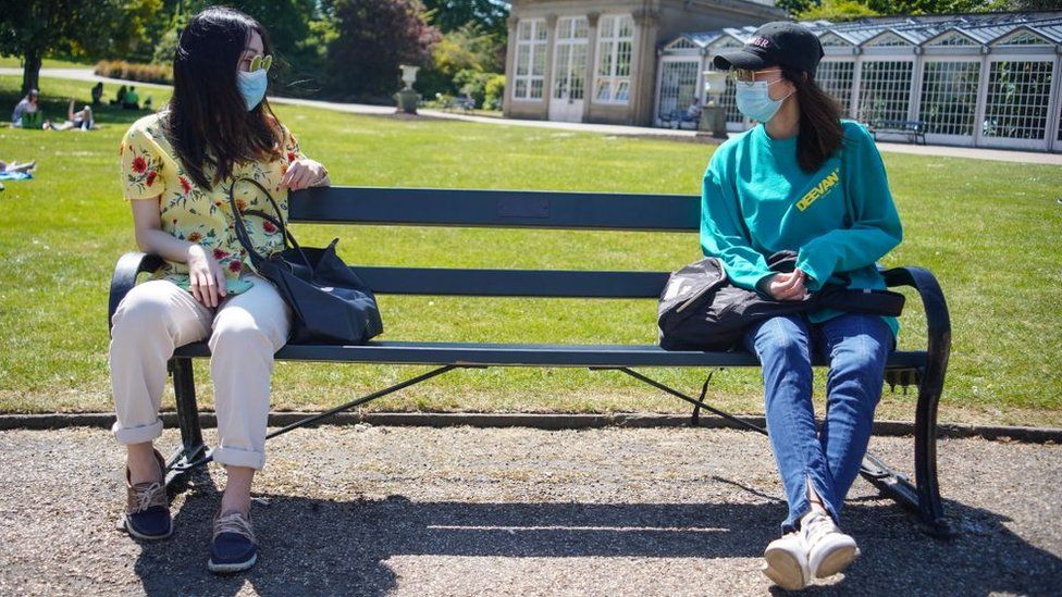 Two people observe social distancing on a bench