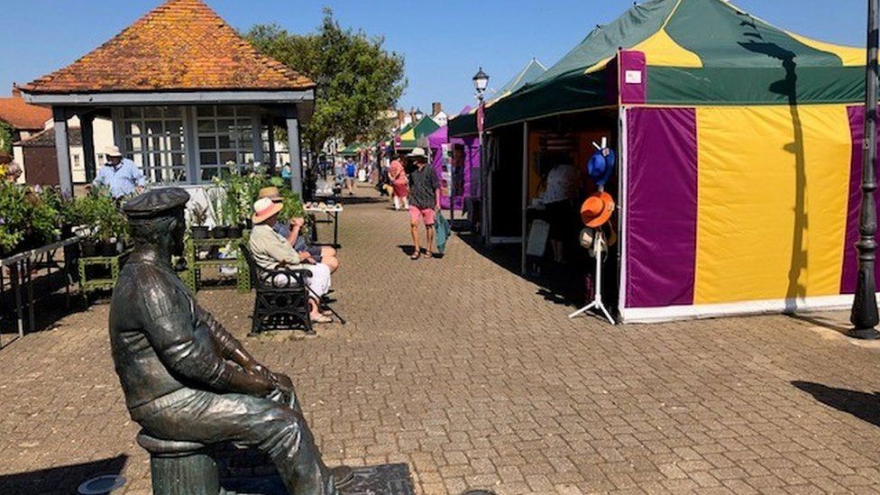 a statue and colourful market stalls on a harbourside on a sunny day