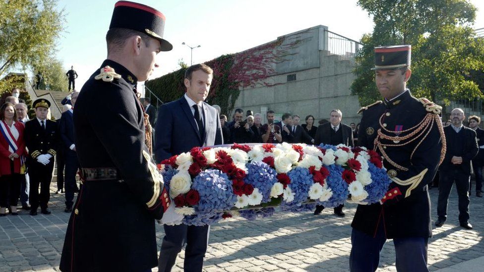 Президент Франции Эммануэль Макрон (в центре) возлагает венок из цветов возле Пон-де-Безон (мост Безона), 16 октября 2021 года в Коломбе, недалеко от Парижа