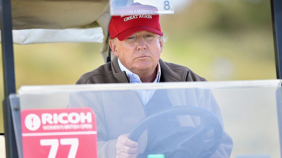 Donald Trump sits behind the wheel of a golf cart.