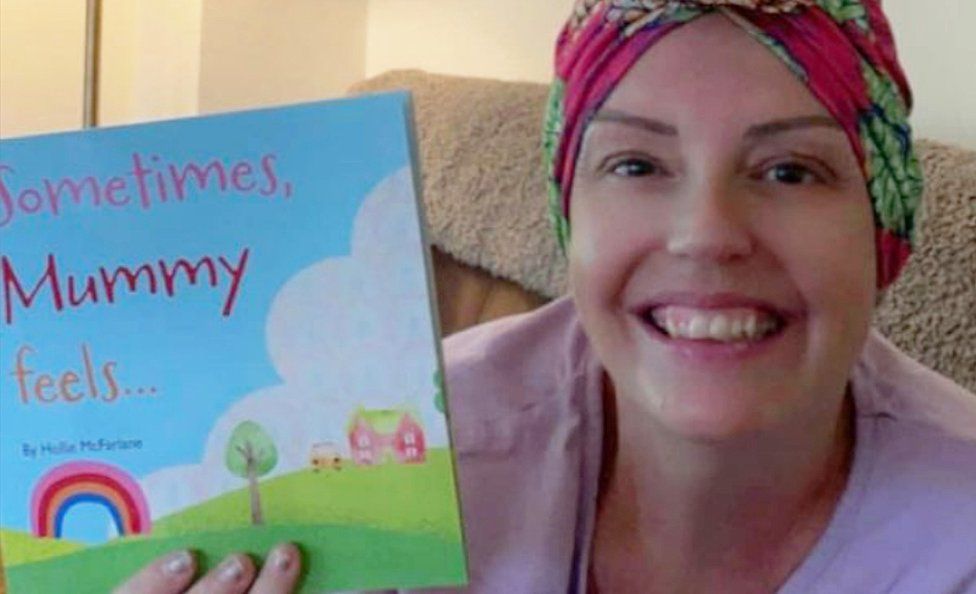 Hollie wearing a headscarf and holding her book titled Sometimes, Mummy feels... with a smile on her face