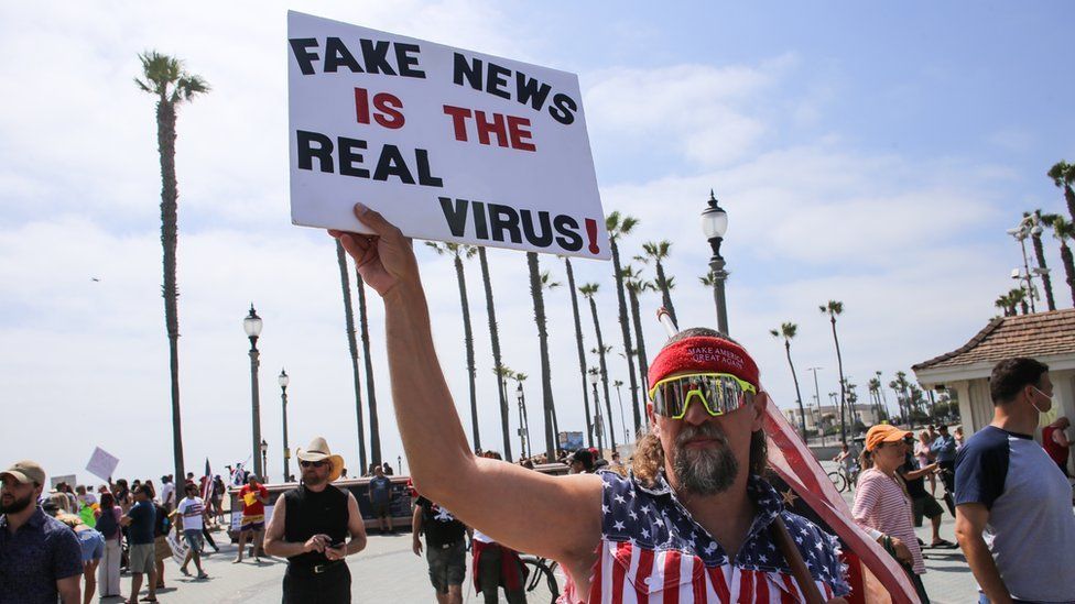 A man holds a sign during a demonstration in California in early May saying "Fake news is the real virus"