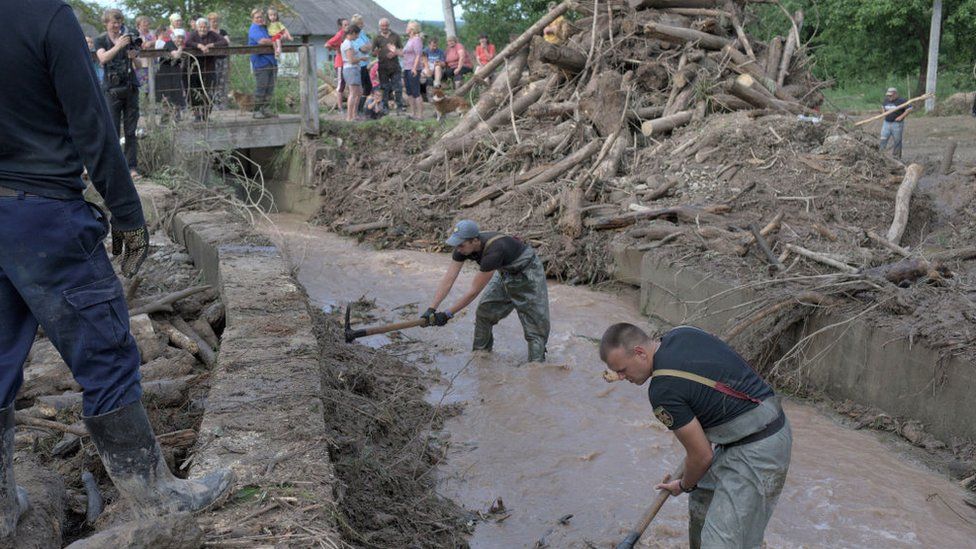Workers clear debris from a channel in a flooded village in western Ukraine, June 2020