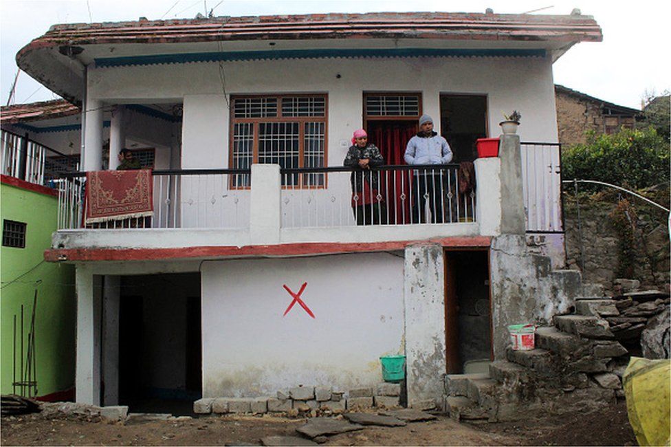 Жители выглядывают с балкона своего поврежденного дома, отмеченного властями знаком «Х» как небезопасного для проживания, в Джошиматхе, в районе Чамоли Уттаракханда, 12 января 2023 г.,