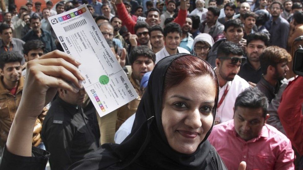 A woman shows a ticket for the upcoming final cricket match of Pakistan Super League while others gather outside a bank to buy tickets in Lahore (01 March 2017)