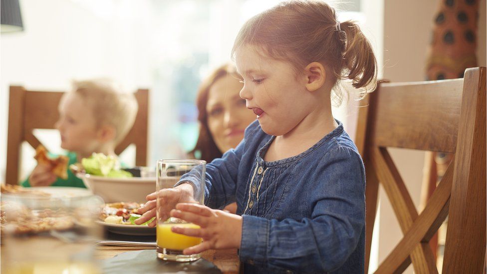 A young girl takes a big drink of orange juice during a meal