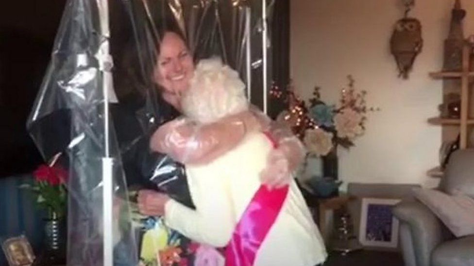 A grandma hugging her granddaughter through a curtain