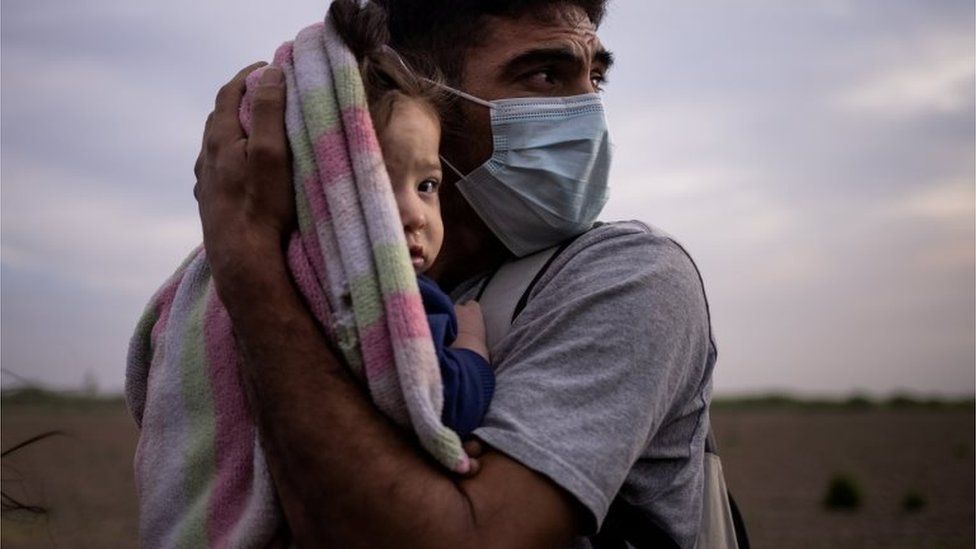 An asylum seeker holds his daughter as they await transportation to a processing centre in the US