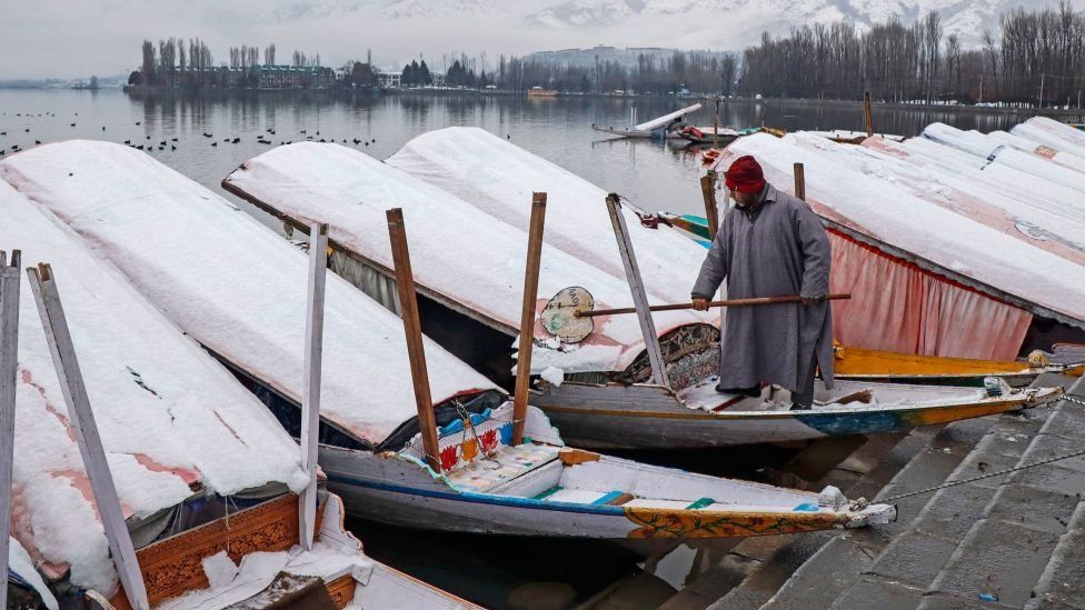 Лодочник убирает снег со своей лодки на озере Дал после снегопада в Шринагаре, 14 января 2023 года.