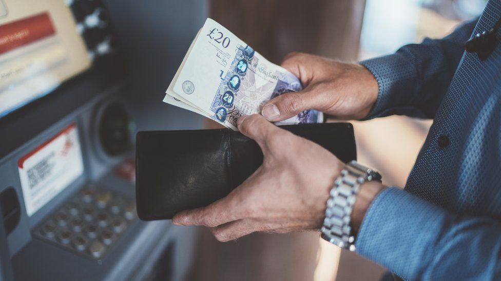 A man putting £20 notes in his wallet