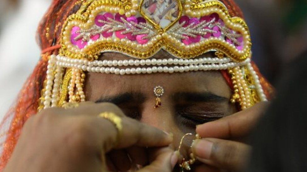 An Indian bride grimaces as a relative adjusts her nose ring during a multi-faith mass wedding in Mumbai on June 22, 2014.