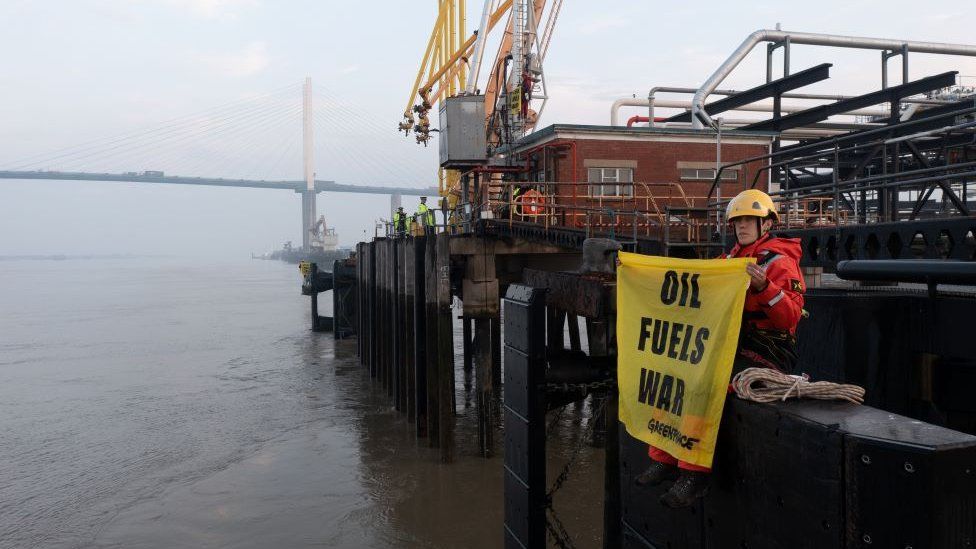 Greenpeace activist with banner that reads foil fuels war