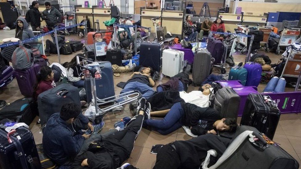 Travellers rest in the Santiago de Chile airport where hundreds of passengers stranded overnight after their flights were cancelled due to curfew imposed in Santiago de Chile