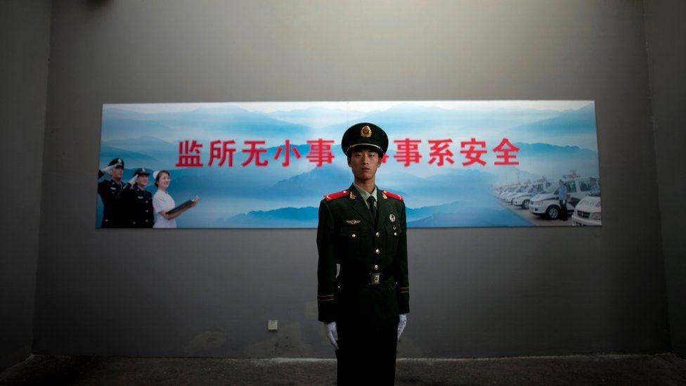 Китайский военизированный полицейский стоит на страже под камерой наблюдения у входа в центр заключения номер два в Пекине