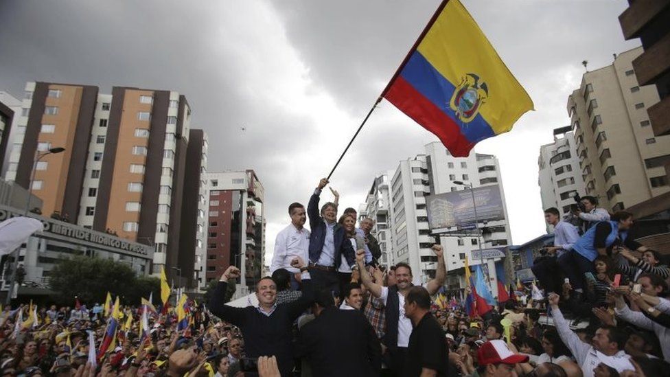 CREO's presidential candidate Guillermo Lasso waves an Ecuadorean national flag, accompanied by his wife Maria de Lourdes Alcivar, his running mate Andres Paez, and surrounded by supporters outside the Electoral National Council, in Quito, Ecuador, Tuesday, Feb. 21, 2017.