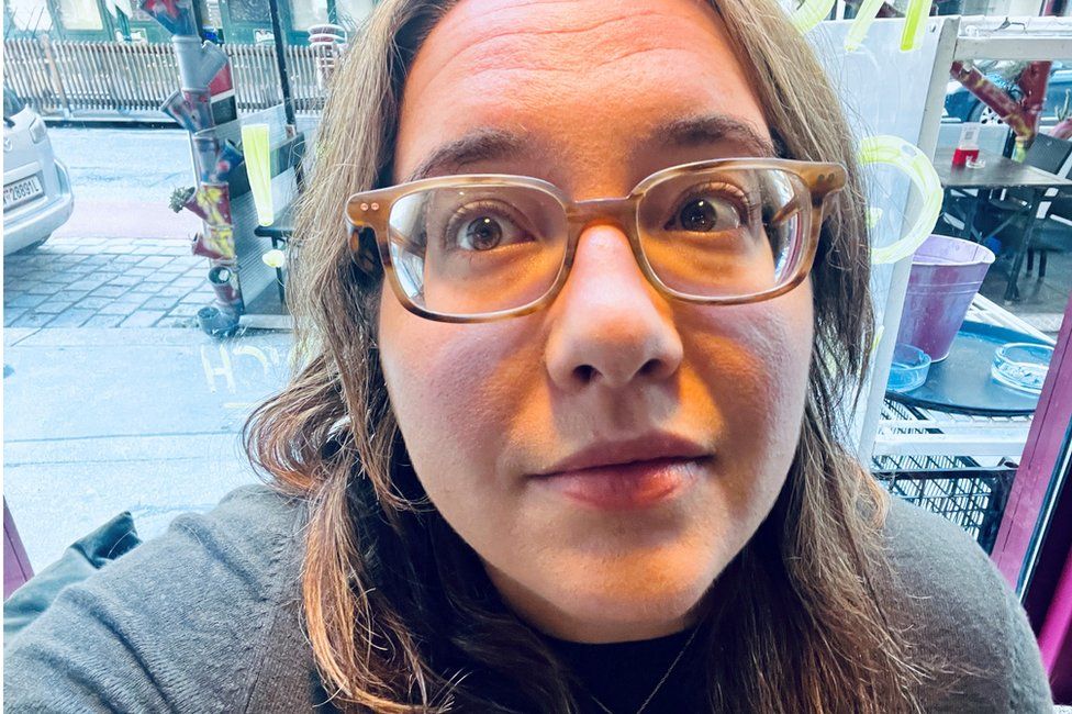 A selfie by Dr Sabrina Mittermeier in a coffee shop in Germany. She is close to the camera and wears glasses and a grey sweater