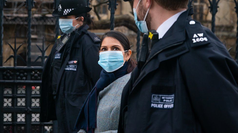 Priti Patel walks with two police officers