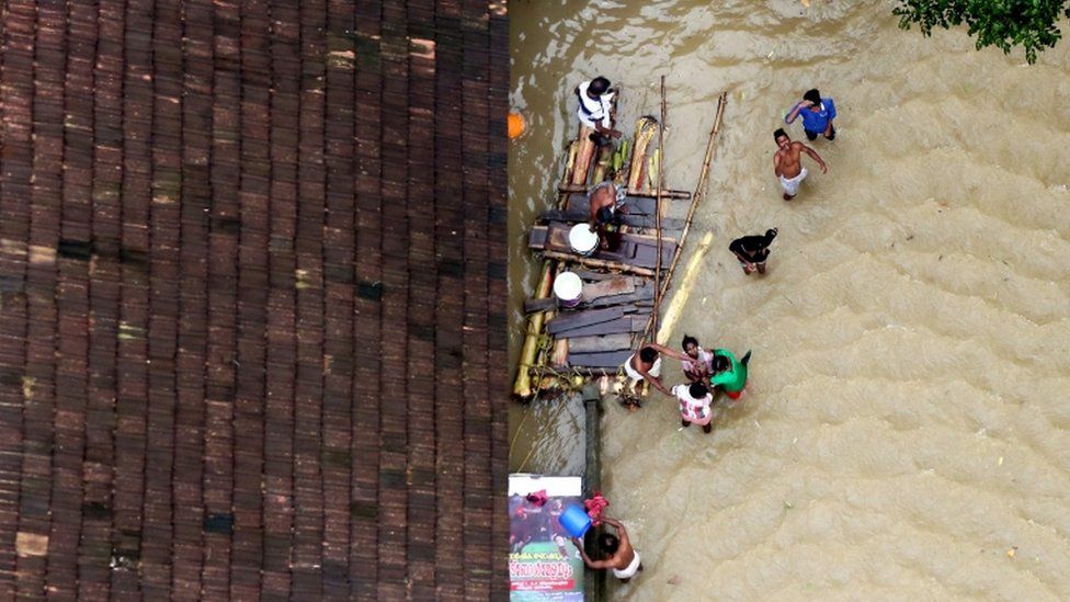 People wait for aid next to makeshift raft at a flooded area in the southern state of Kerala, India,