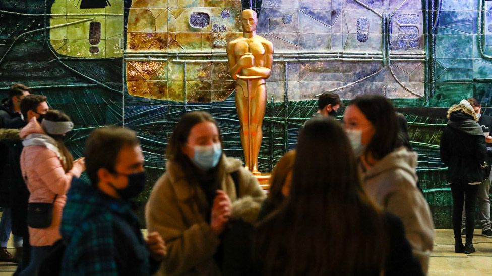 Cinema fans in masks in front of an Oscars statue