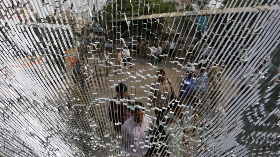 People are seen through the broken glass of a passenger bus that was damaged in clashes between members of the Patel community and the Dalit community during a protest rally in Ahmedabad, India, August 25, 2015
