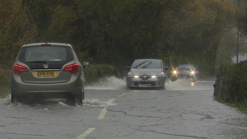 Vehicles drive along a road with surface water