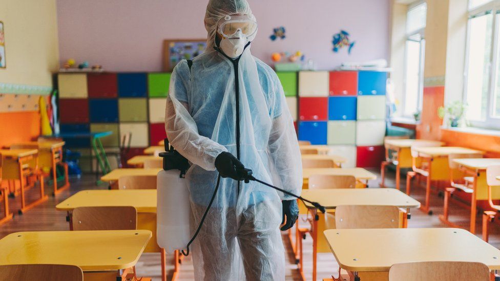 Stock: Man in protective suit disinfecting school building