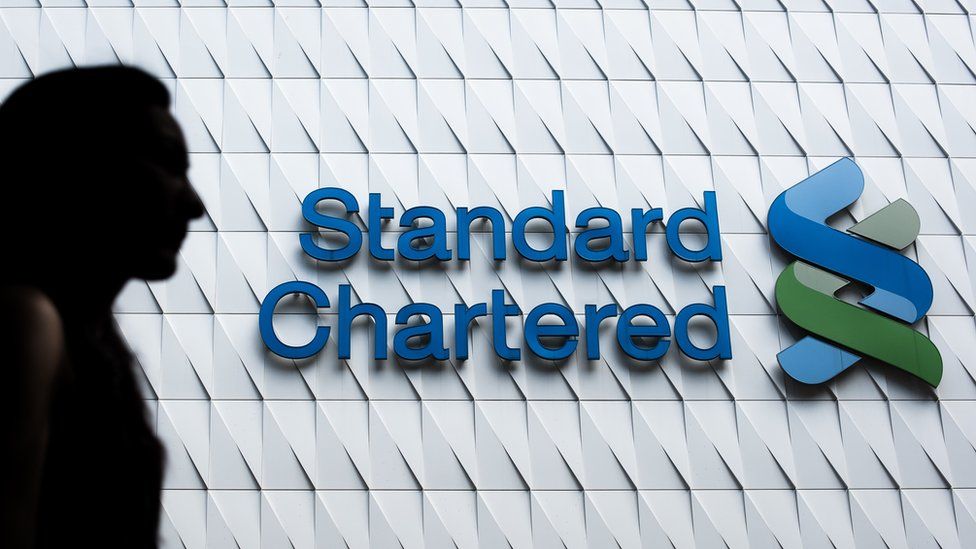 A woman walks past a logo of the Standard Chartered bank in Hong Kong on August 5, 2015