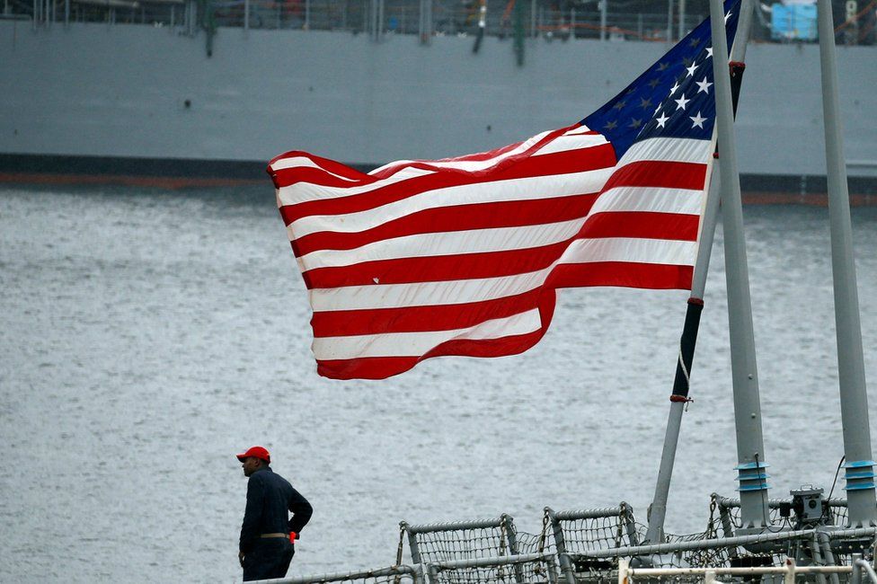 A member of the U.S. Navy Damage Control Training Team is seen near the U.S. national flag on the Arleigh Burke-class guided-missile destroyer USS Fitzgerald, which has been damaged from colliding with a Philippine-flagged merchant vessel, at the U.S. naval base in Yokosuka, south of Tokyo, Japan 18 June 2017