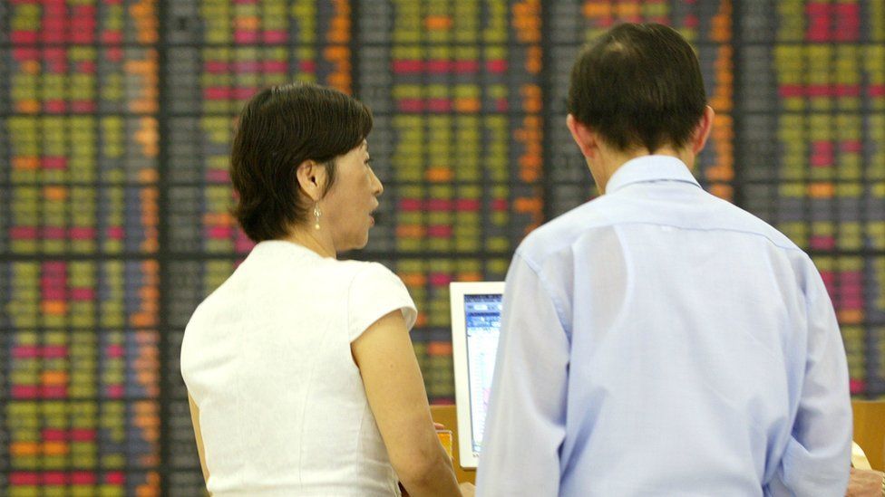 People look at stock market boards in Asia