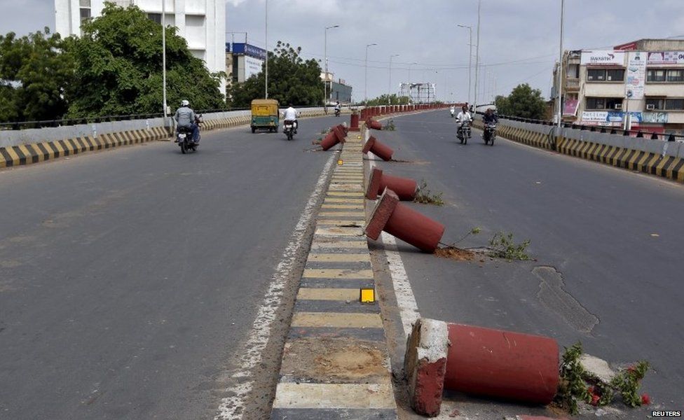 Vehicles travel past flower pots installed on a road divider which were damaged in the clashes between the police and protesters in Ahmedabad, India, August 26, 2015