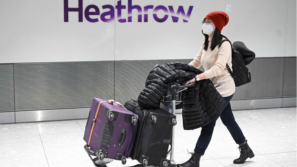 A woman pushing luggage through Heathrow airport