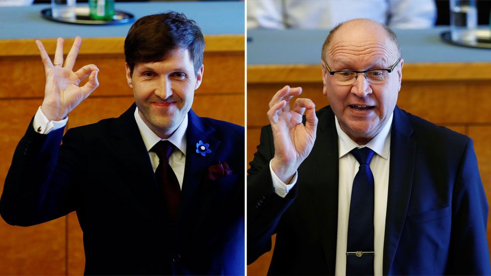 A composite image shows Martin Helme (L) and Mart Helme make the "OK" hand gesture with thumb and forefinger closed, other fingers extended, in a parliament chamber