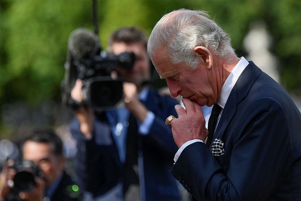 King Charles looks at floral tributes left to his late mother, the Queen